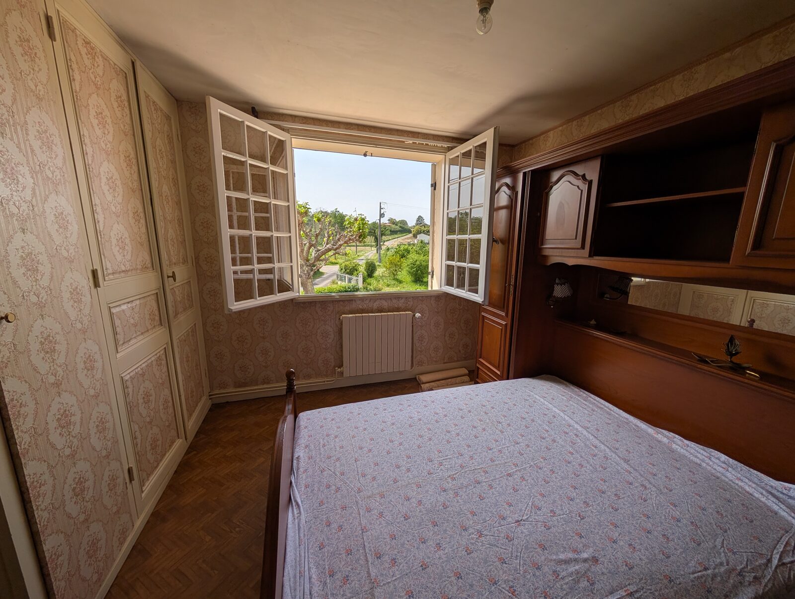 Chambre avec papier peint fleuri et vue sur la campagne